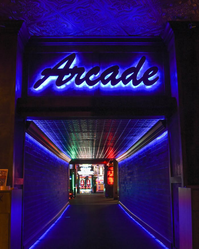 who-we-are Vibrant neon light hallway leading to retro arcade gameplay area.