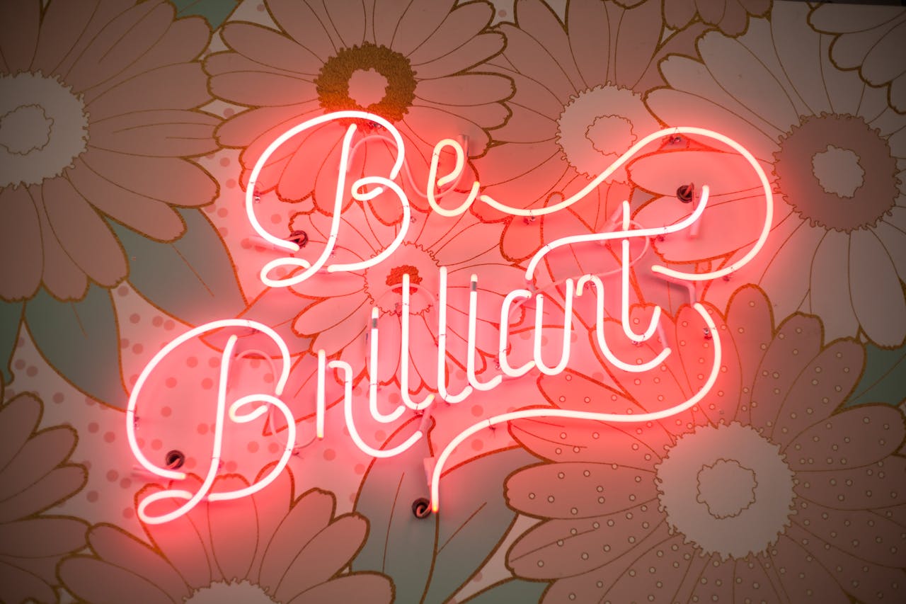 services-01 A glowing neon sign reading 'Be Brilliant' against a floral backdrop creates a vibrant and motivational atmosphere.